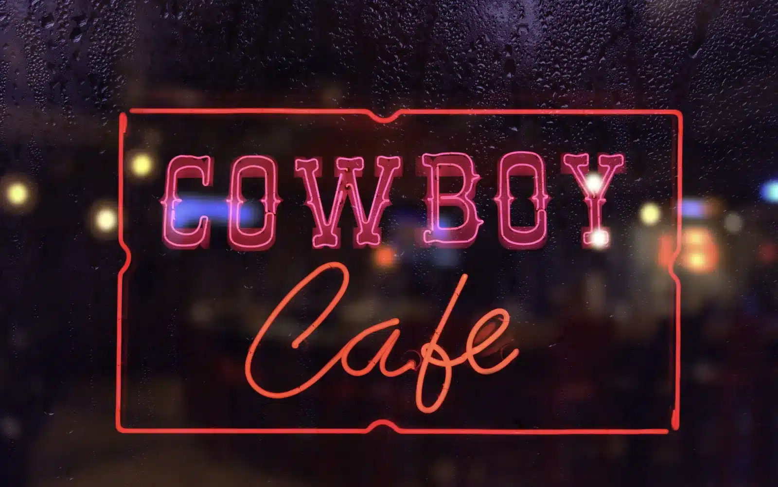 Neonbord met de tekst Cowboy Cafe achter een raam met regendruppels